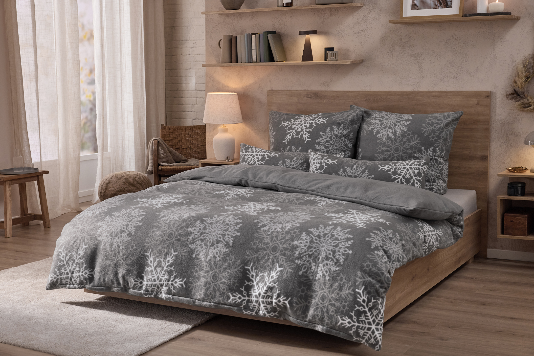 Hubane magamistuba voodiga, mis on kaetud halli lumehelvestega tekiga, ja öökappidega.