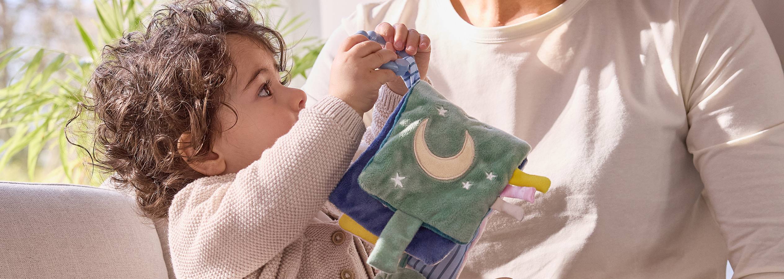 Väike laps hoiab käes armsat helendavat kuu ja tähtedega pehmet mänguasja.