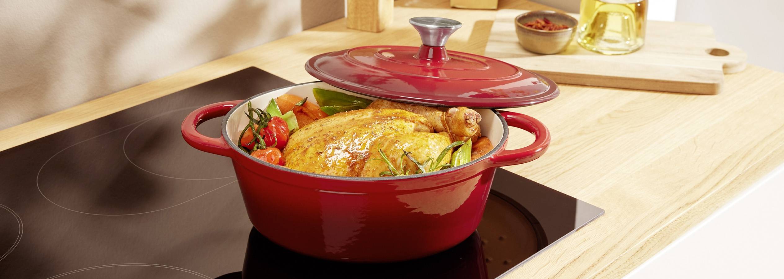 Красная чугунная кастрюля с запеченной курицей и овощами на индукционной плите