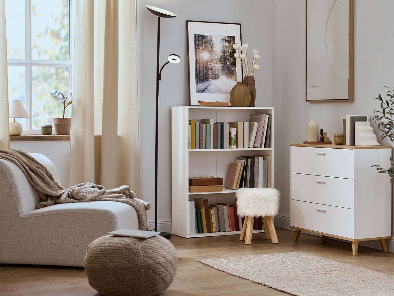 Hubane elutuba tugitooli, raamaturiiuli ja kummutiga neutraalsetes toonides.