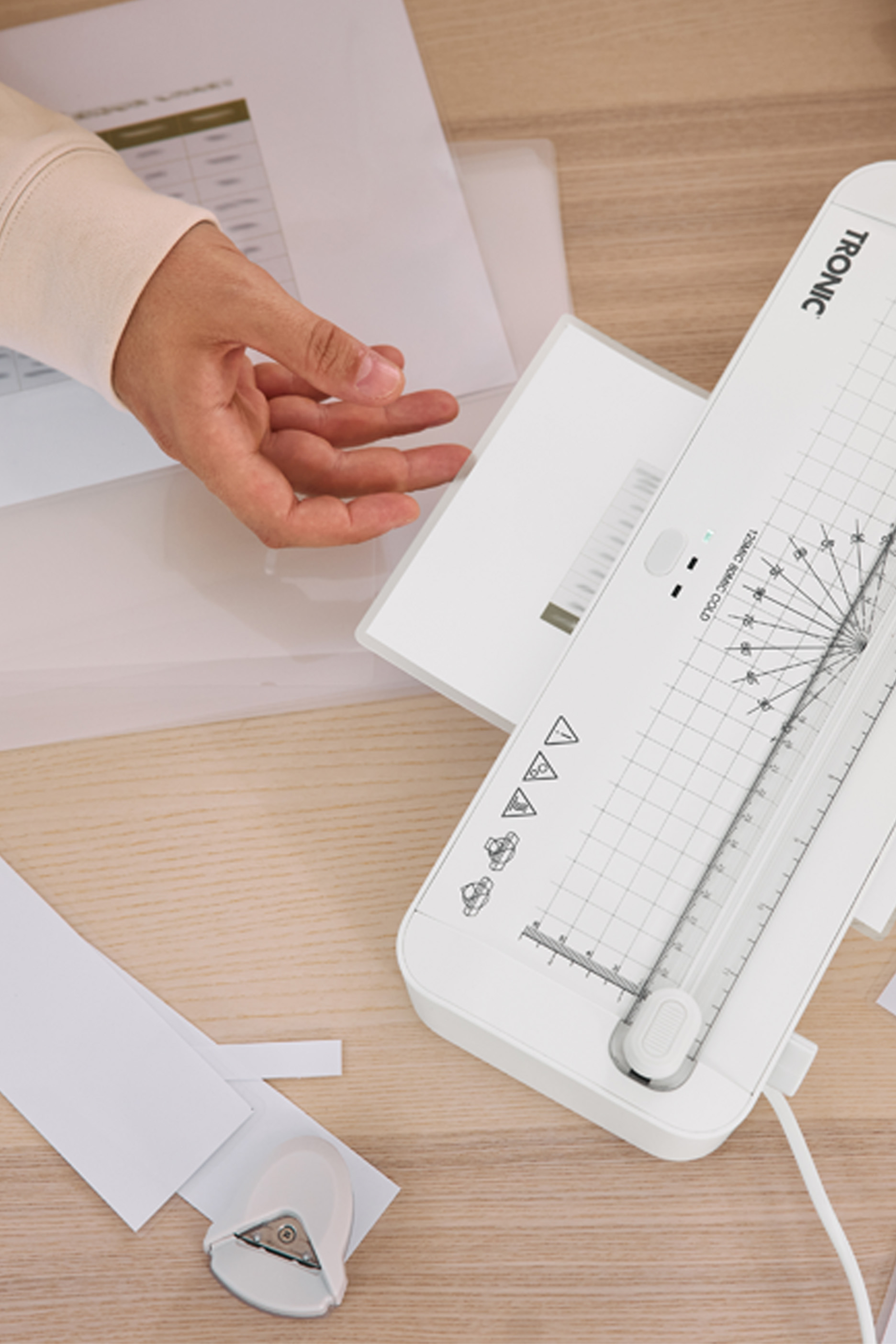 Inimese käsi, Tronic laminaator, paber ja nurgalõikur puidust laual.