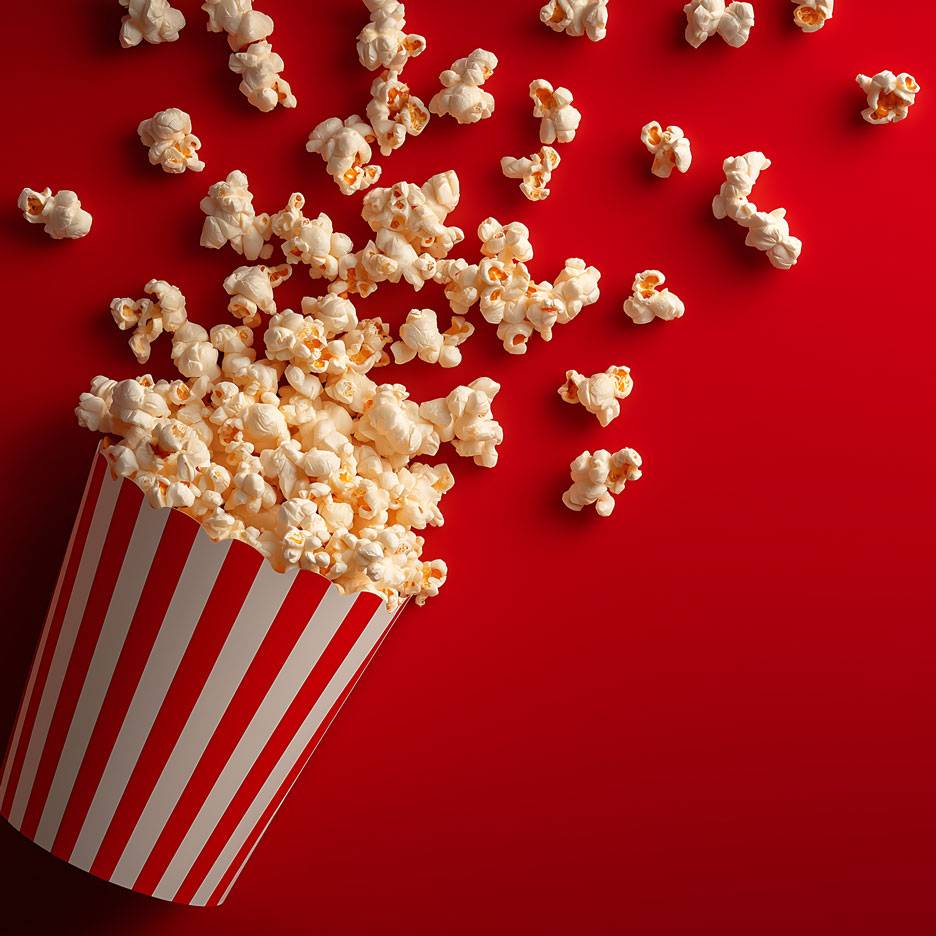 Popkorn punasel taustal, osa popkornist triibulises papptopsikus.