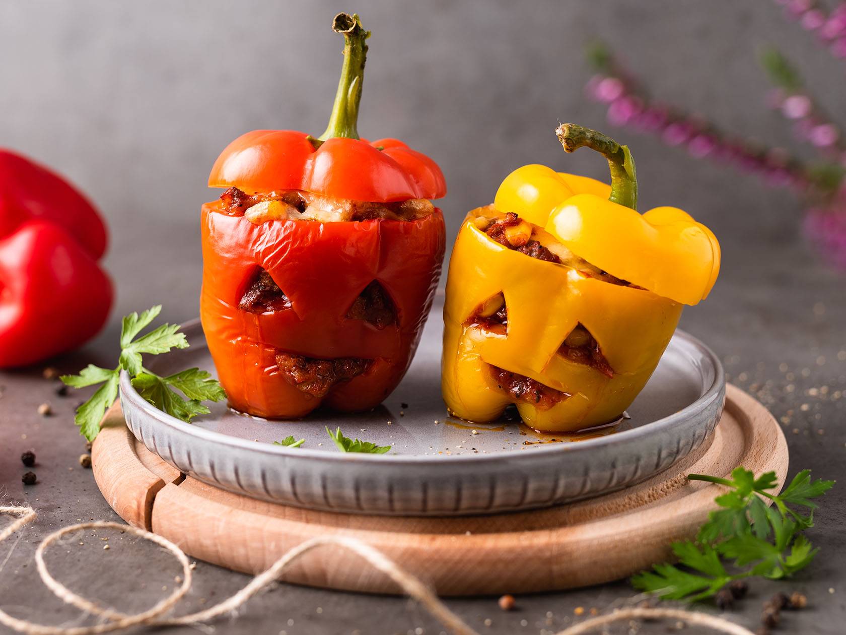 Kaks Halloweeni teemalise näoga täidetud paprikat hallil taldrikul.