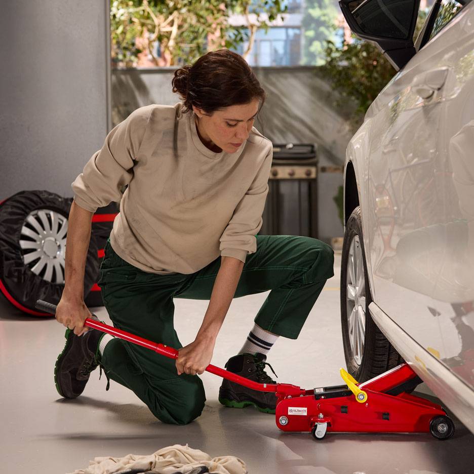 Naine kasutab punast hüdraulilist tungrauda valge auto tõstmiseks, läheduses varuratas.