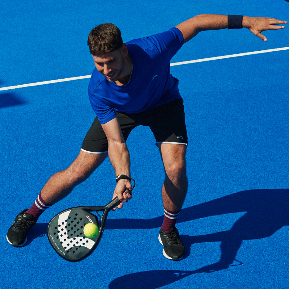 Mees sinises T-särgis ja mustades lühikestes pükstes mängib padelit reketi ja palliga.