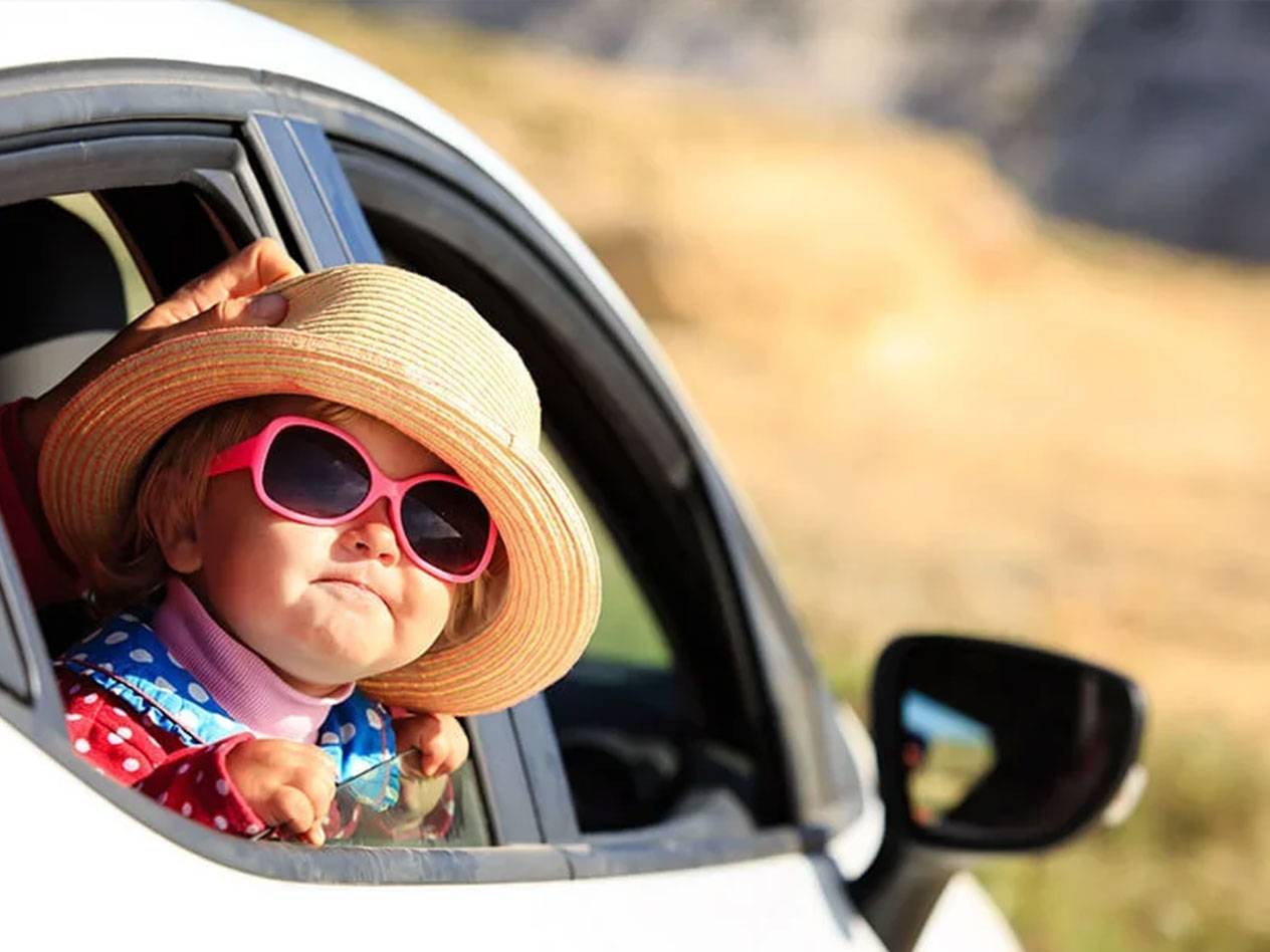 Väike laps mütsiga ja päikeseprillidega autos.