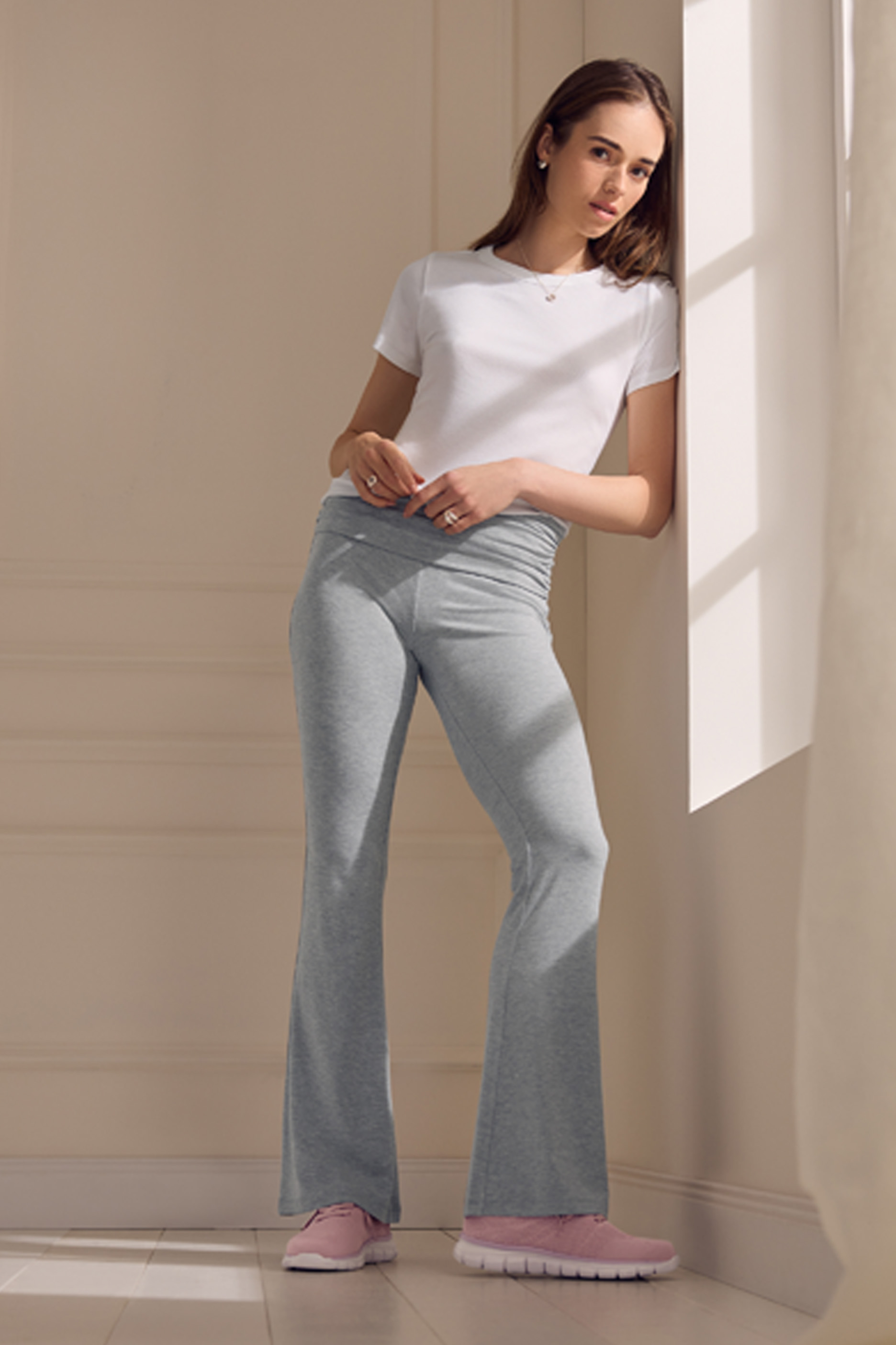 Naine valges T-särgis ja hallides dressipükstes, roosad tossud.